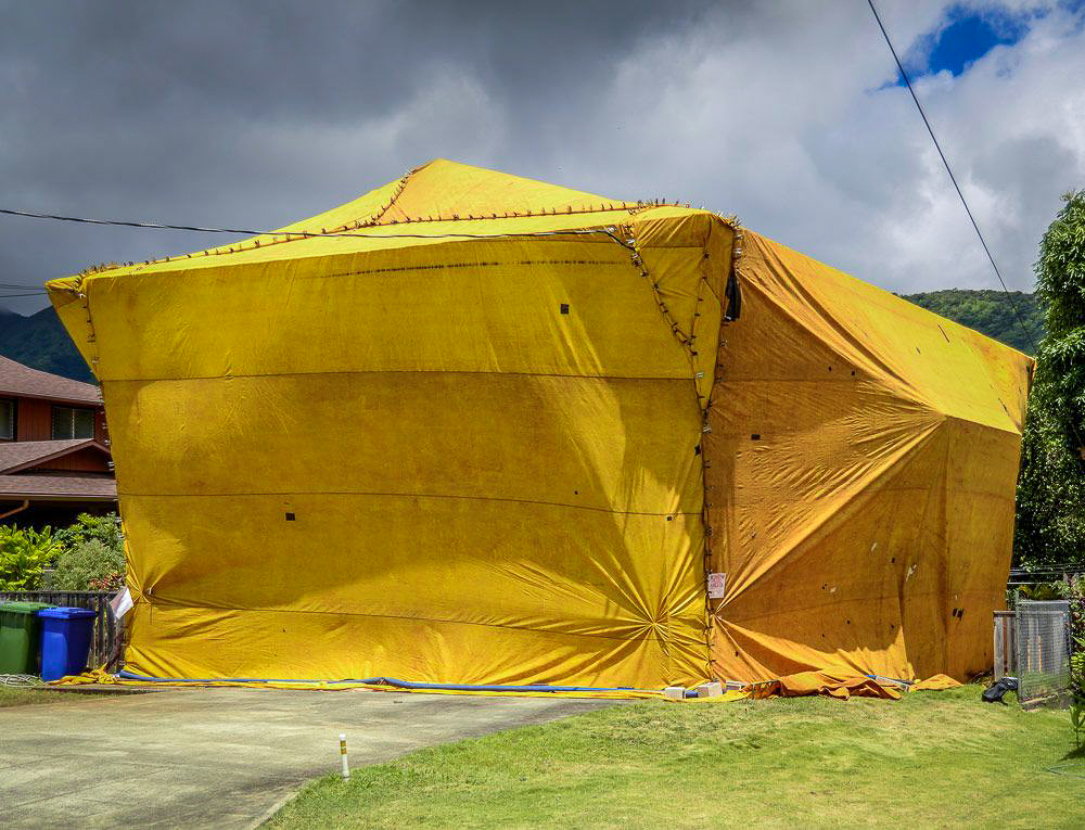 Home sealed under yellow fumigation tarps with warning signage